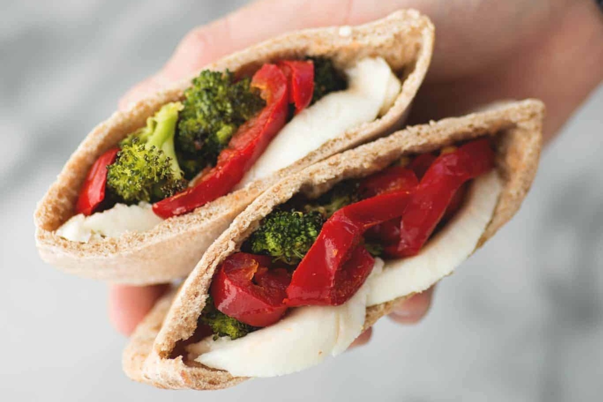 A person is holding a pita with broccoli and peppers while exploring new broccoli recipes.
