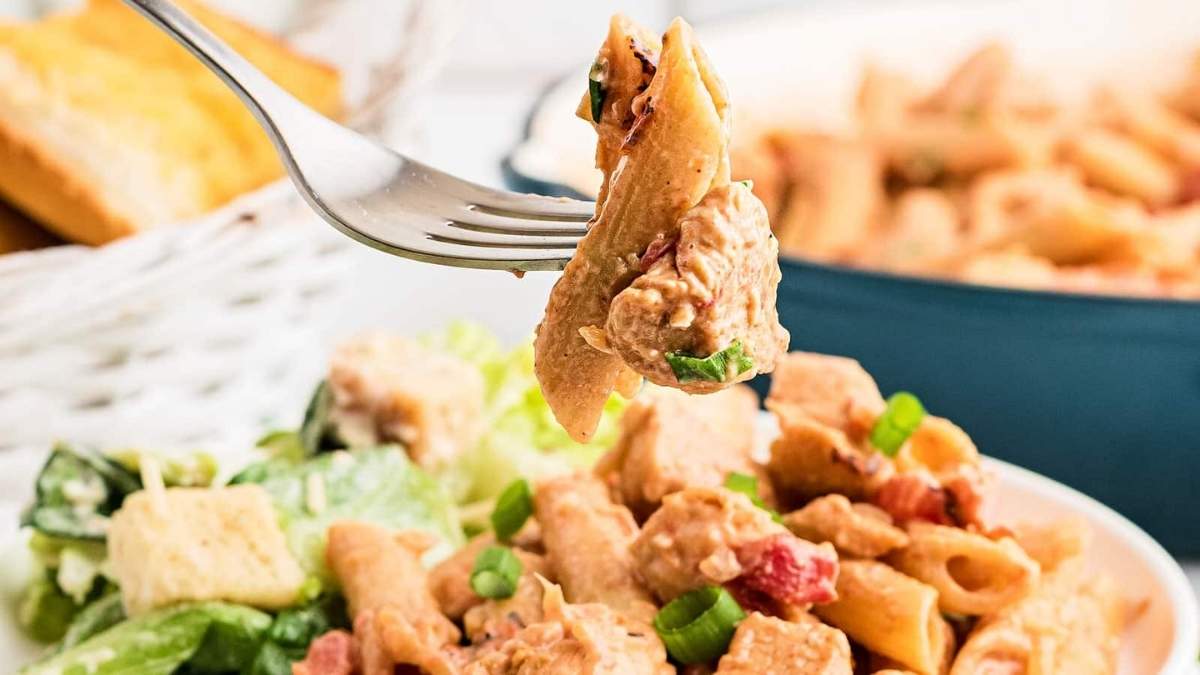 A fork is being used to pick up a bowl of comfort food pasta salad.