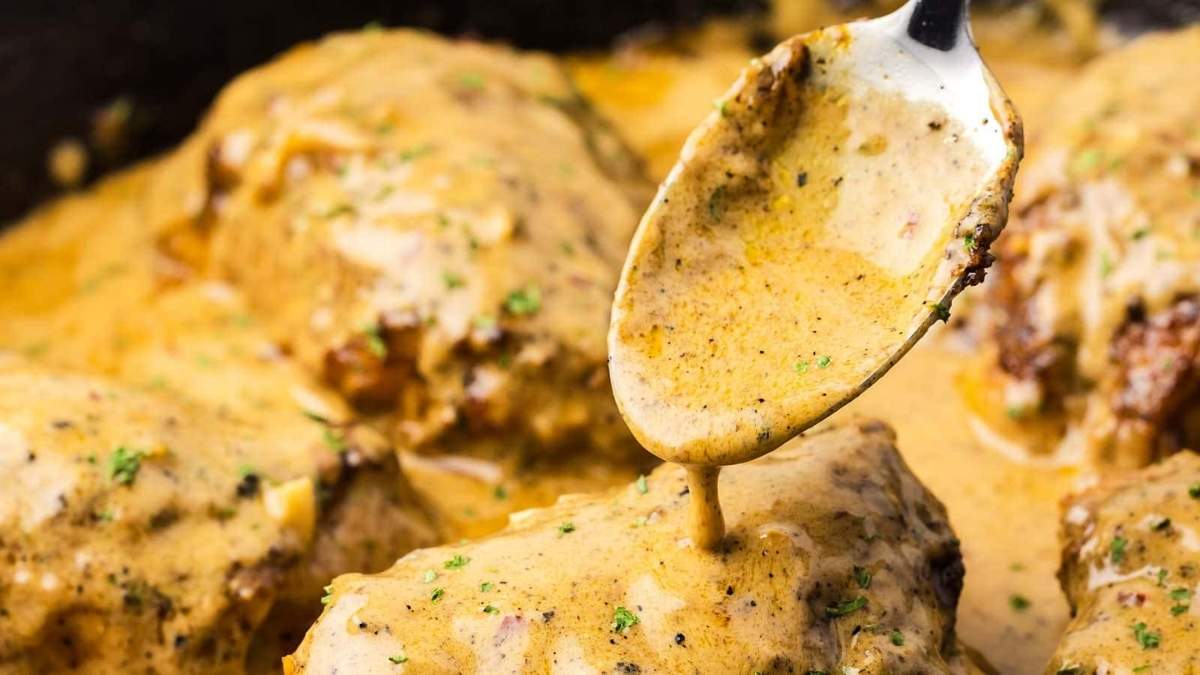 A spoon is being used to drizzle sauce over chicken in a skillet.