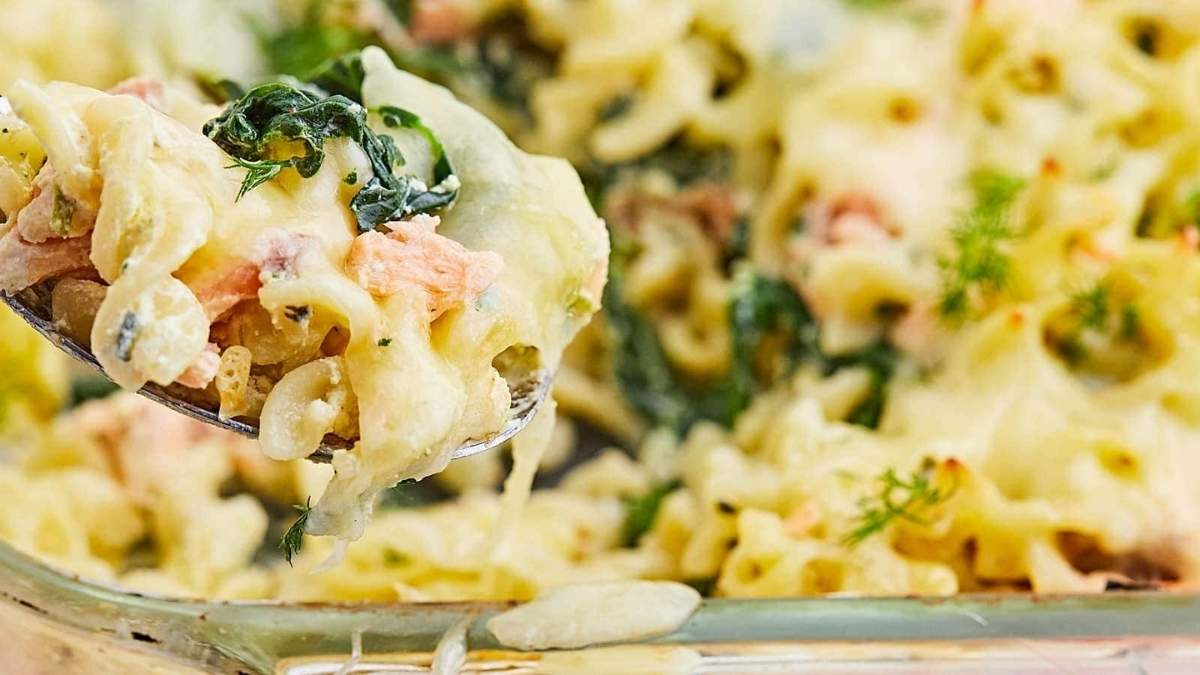 A comfort food recipe featuring a spoon lifting up pasta with salmon and spinach.