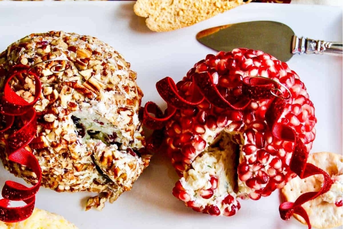 Two festive cheese balls adorned with cranberries and nuts on a plate.
