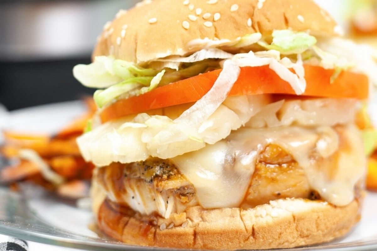 A mouth-watering chicken burger is presented on a plate accompanied by crispy fries. (Main Dishes)