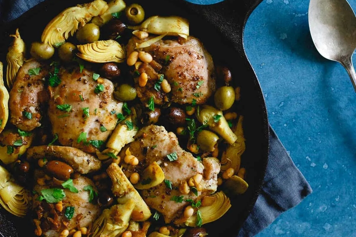 Chicken thighs with artichokes and olives in a skillet.