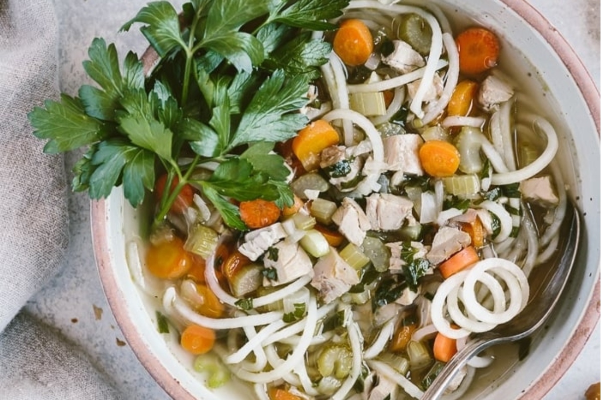 A bowl of chicken noodle soup with carrots and parsley.