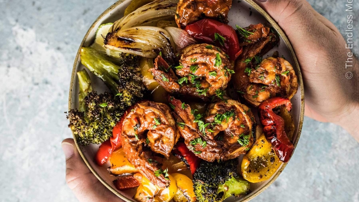 A person enjoying a dinner of shrimp and vegetables, holding a bowl.