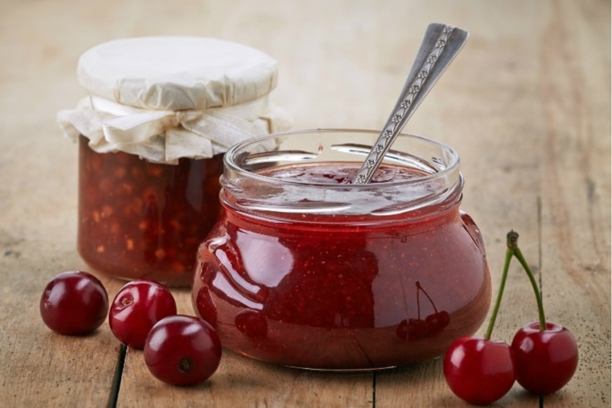 Two jars of cherry jam, perfect as gifts, on a wooden table.
