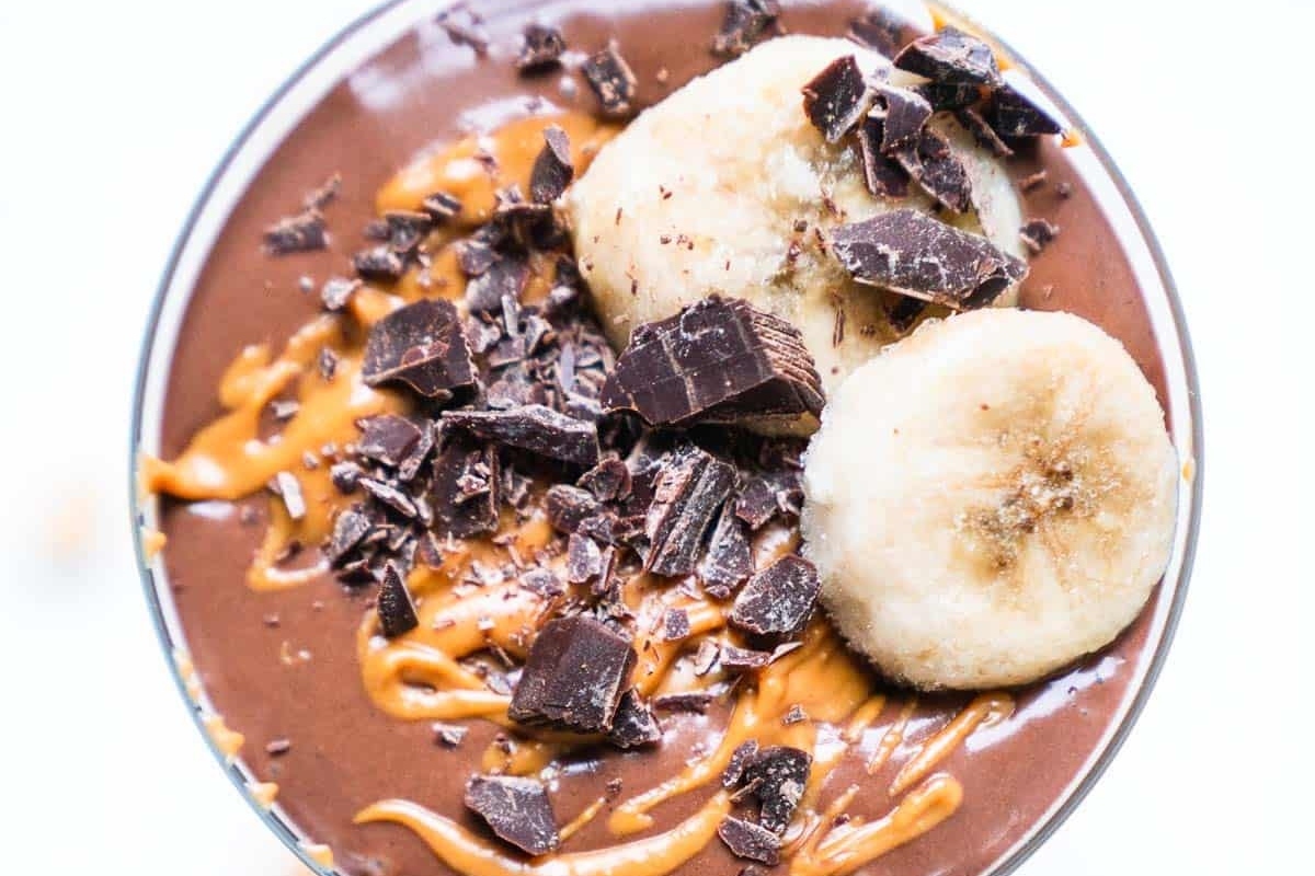 A healthy, high protein breakfast smoothie featuring a chocolate banana base and toppings of chocolate chips and banana slices.