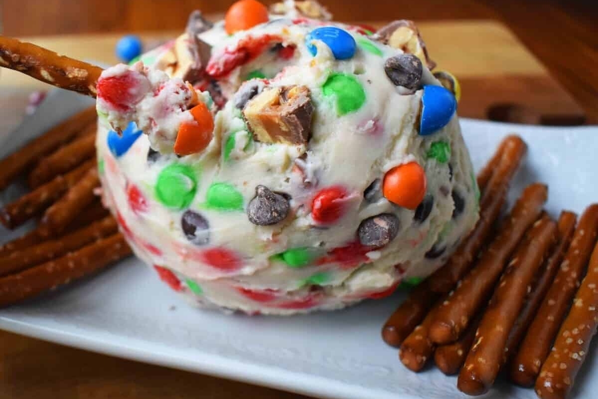 A Festive apple covered in candy and pretzels on a plate.