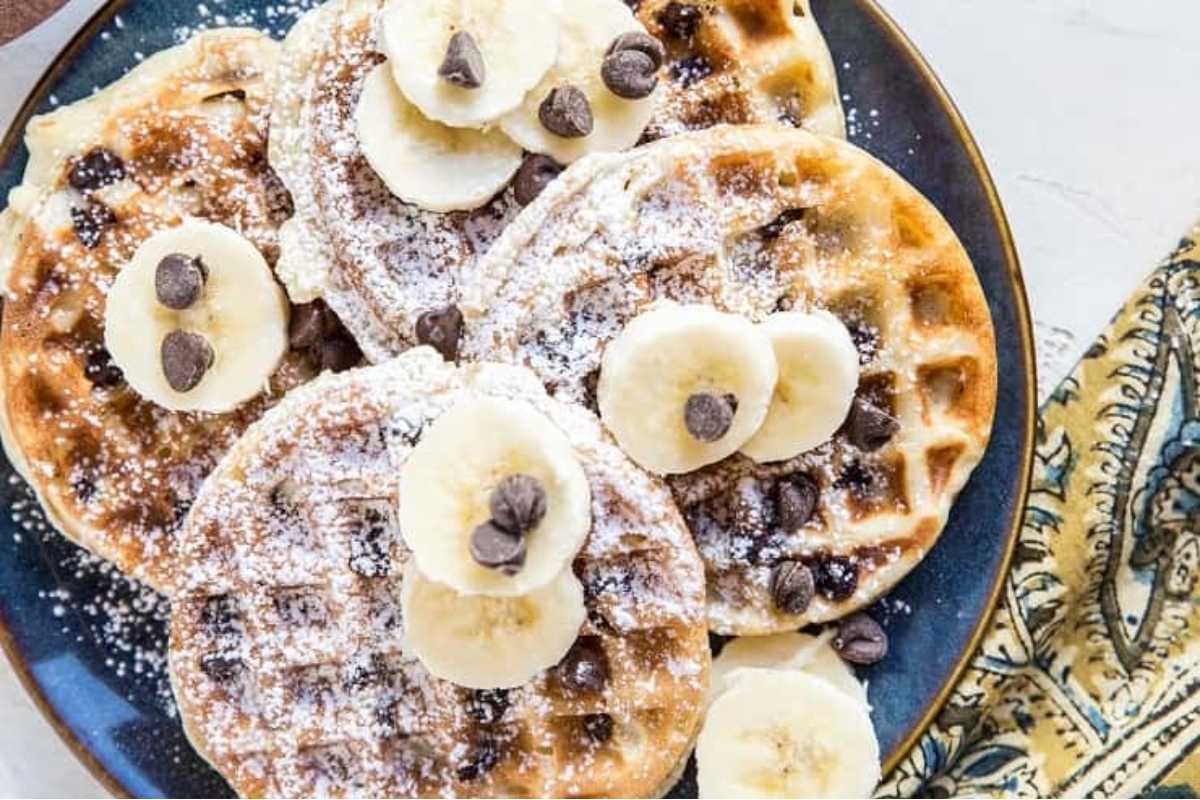A delightful recipe for chocolate chip waffles served on a plate, topped with ripe bananas.