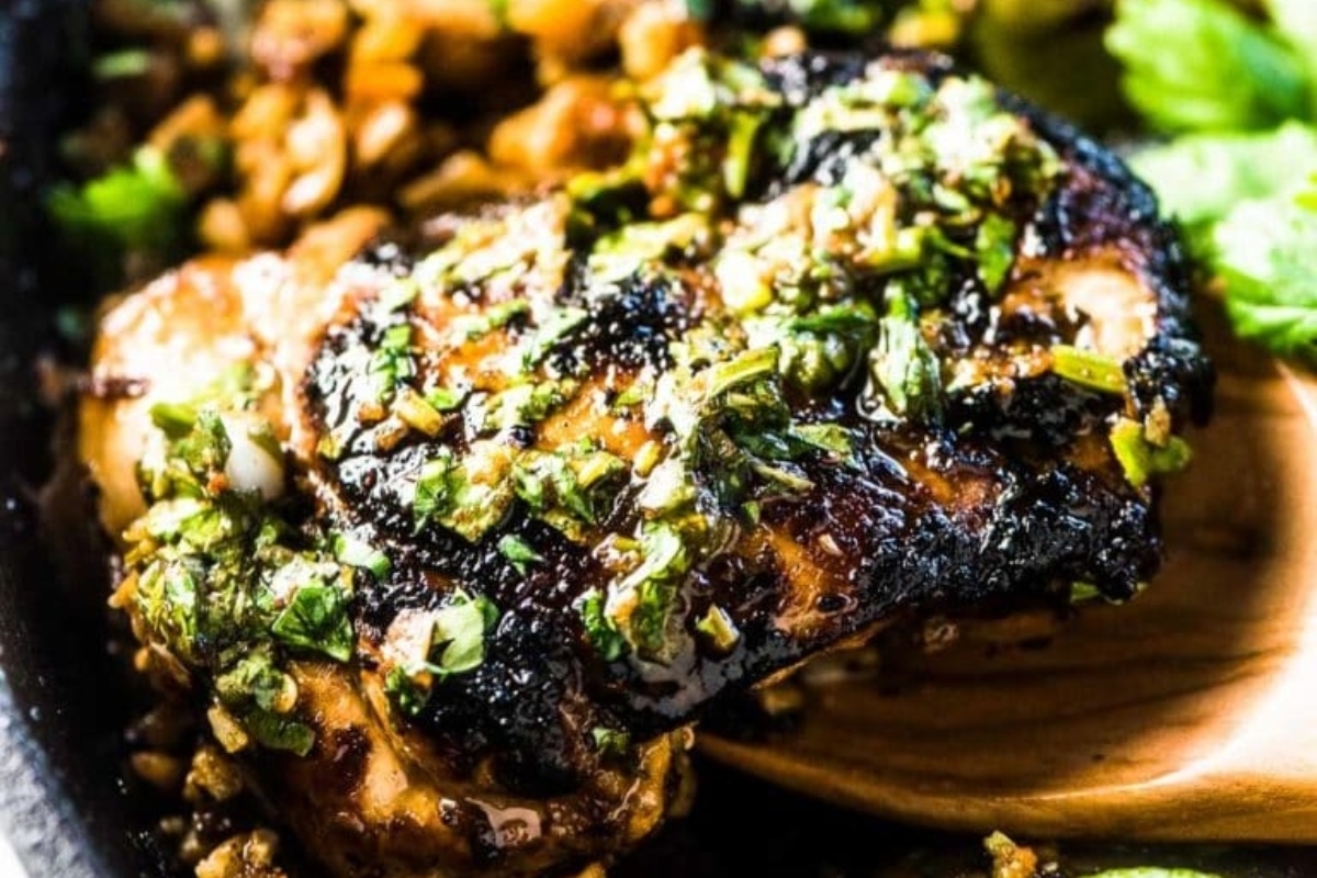 A skillet with chicken thighs and greens in it.