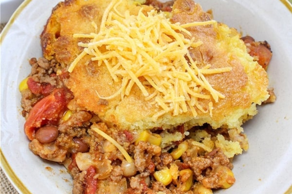 A comforting bowl of cheesy cornbread loaded with meat and smothered in melted cheese, perfect for serving alongside a steaming bowl of chili.