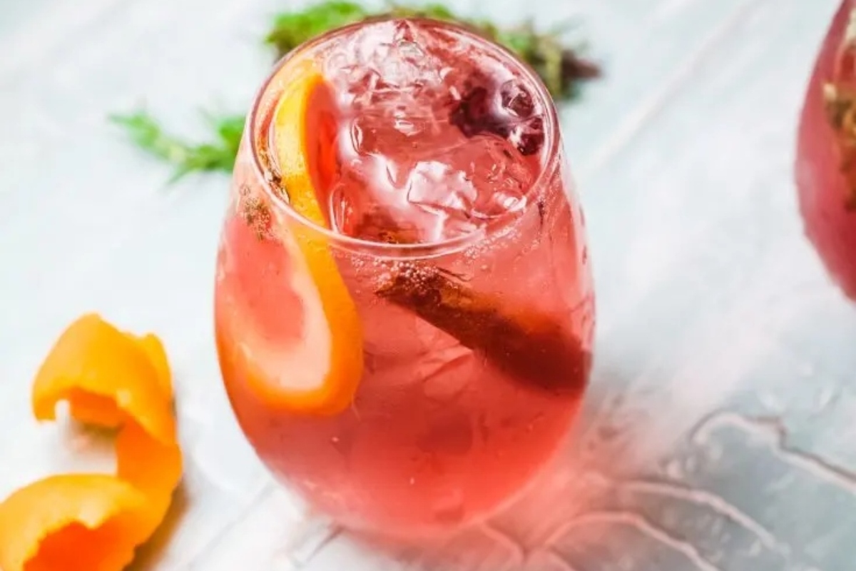 A romantic Valentine's Day cocktail featuring a pink drink adorned with orange slices and a sprig of thyme.