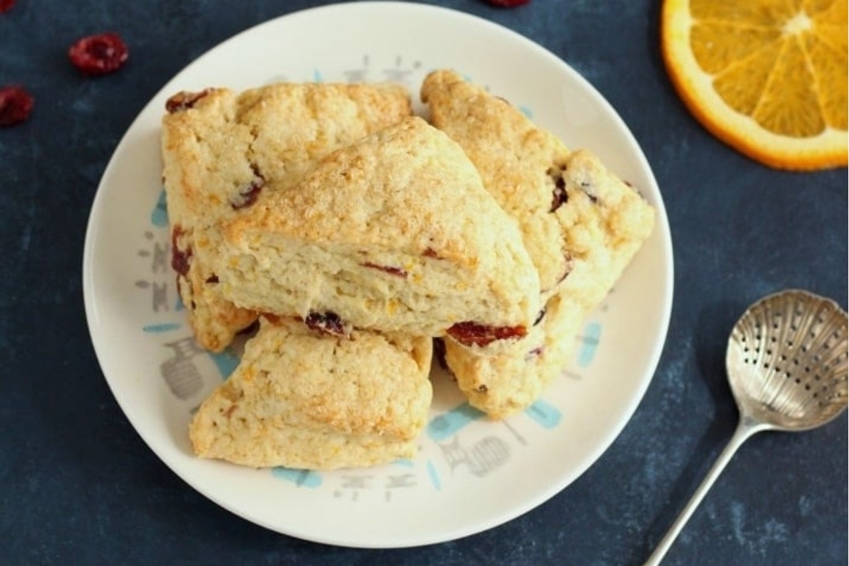 Cranberry scones on a plate with orange slices, perfect for a refreshing snack.