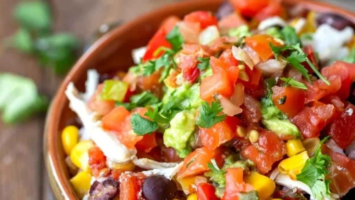 A bowl of Mexican corn salad on a wooden table topped with tender chicken cooked in a slow cooker.