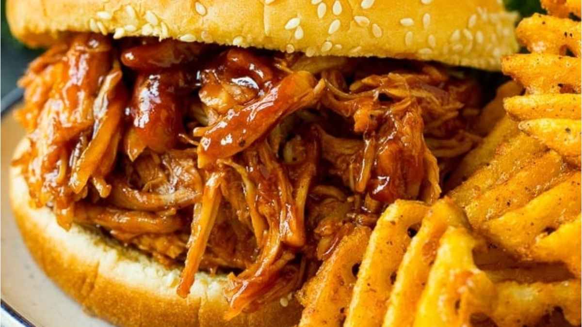A slow cooker pulled pork sandwich with fries on a plate.