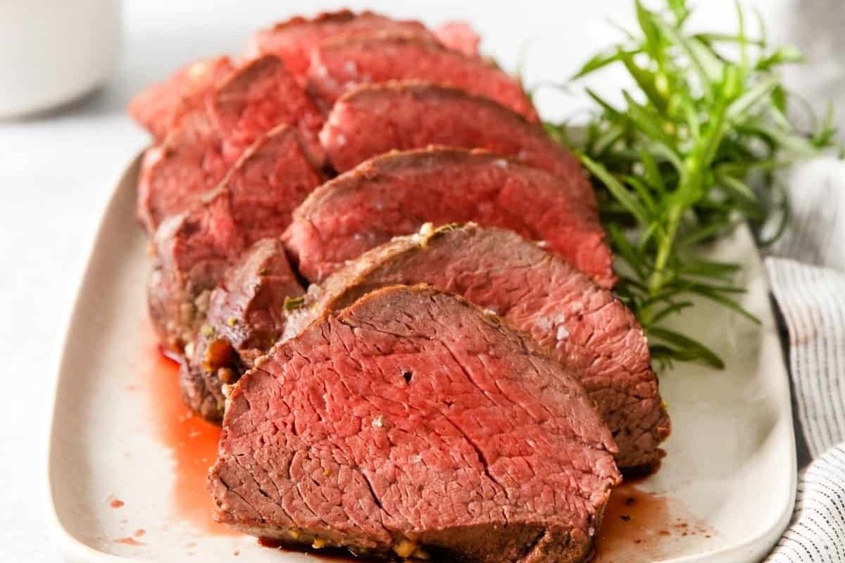 Christmas dinner featuring beef tenderloin on a white plate with rosemary sprigs.