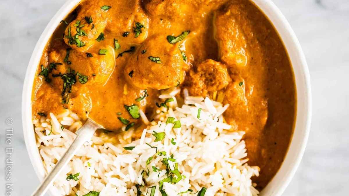 A slow cooker chicken curry served with rice and a spoon.