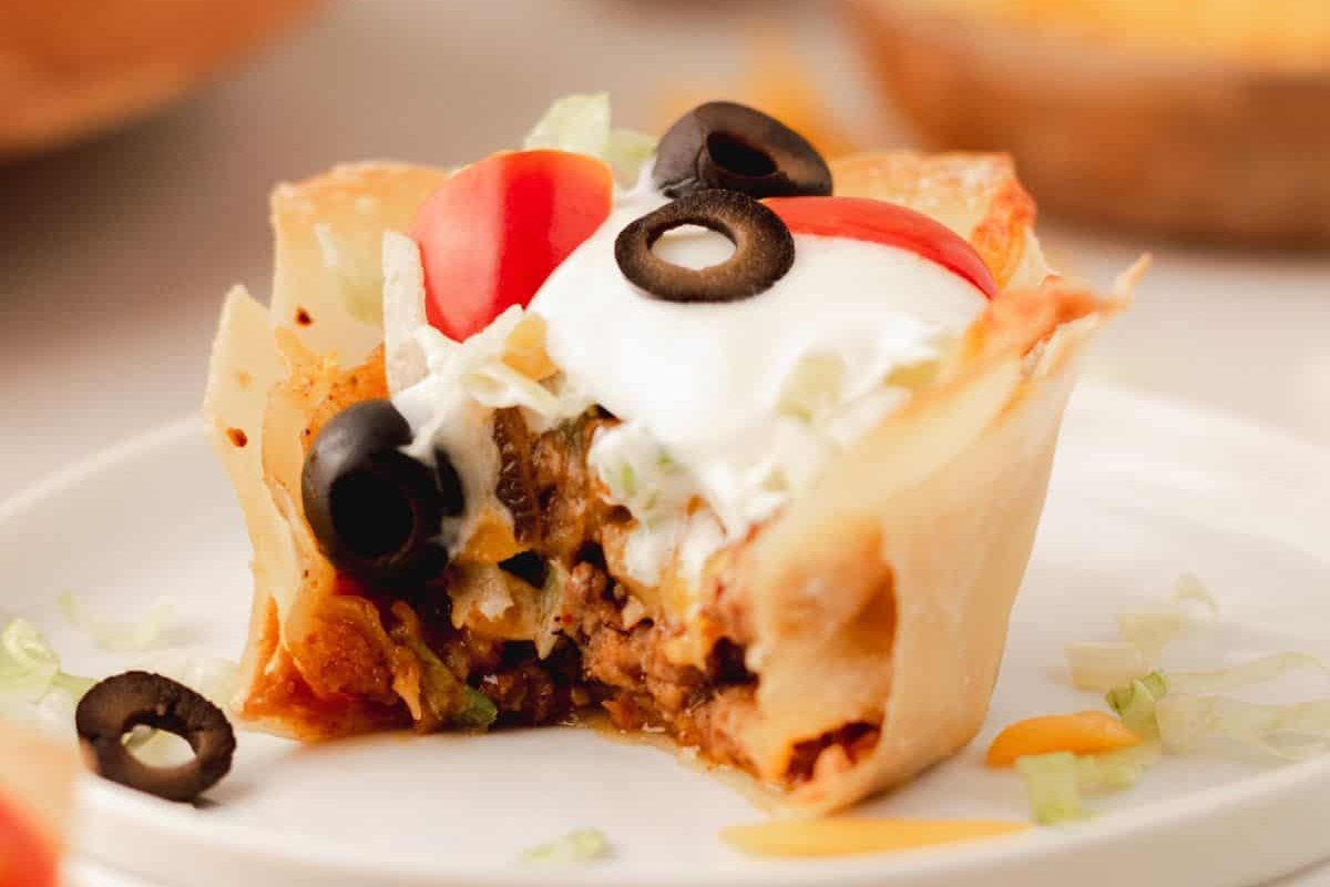 Bite-sized Mexican taco cups, perfect for game day, topped with sour cream and olives on a plate.