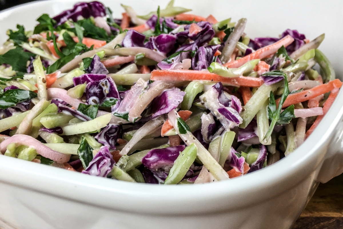 Coleslaw with broccoli in a white bowl on a wooden table.
