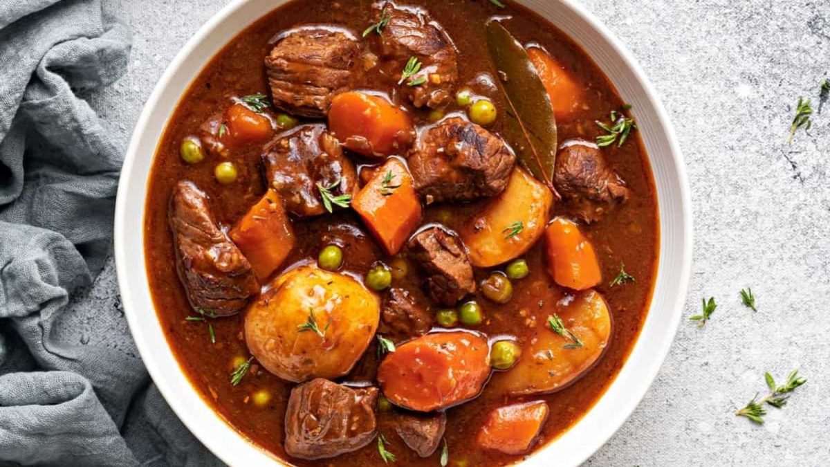 Beef stew in a white bowl with carrots and potatoes.