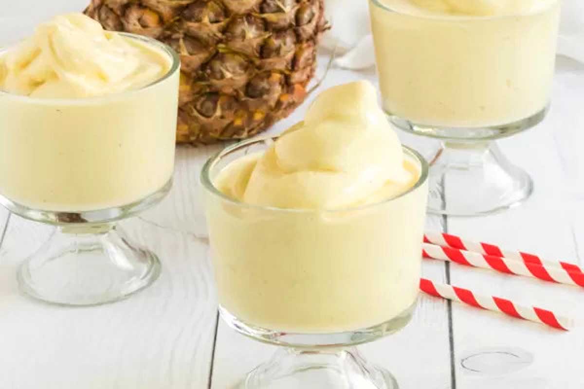 Three Hawaiian-inspired glasses of pineapple ice cream with a pineapple in the background.