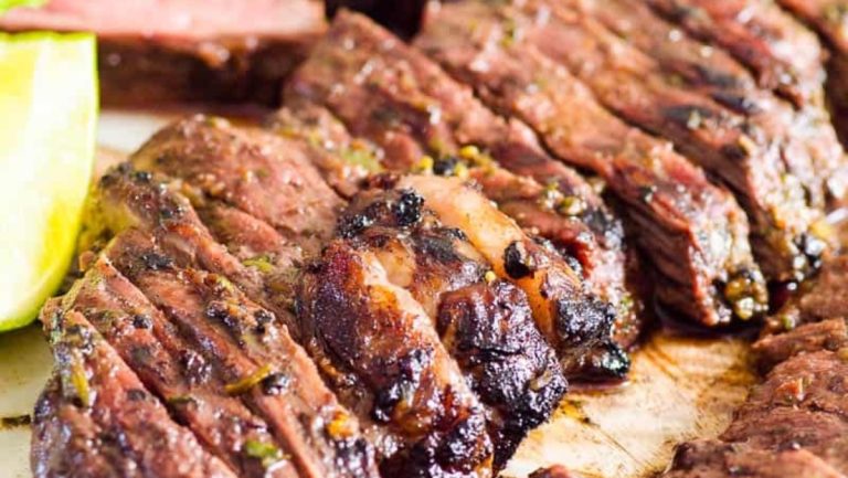Sizzling beef steak on a cutting board garnished with lime wedges.