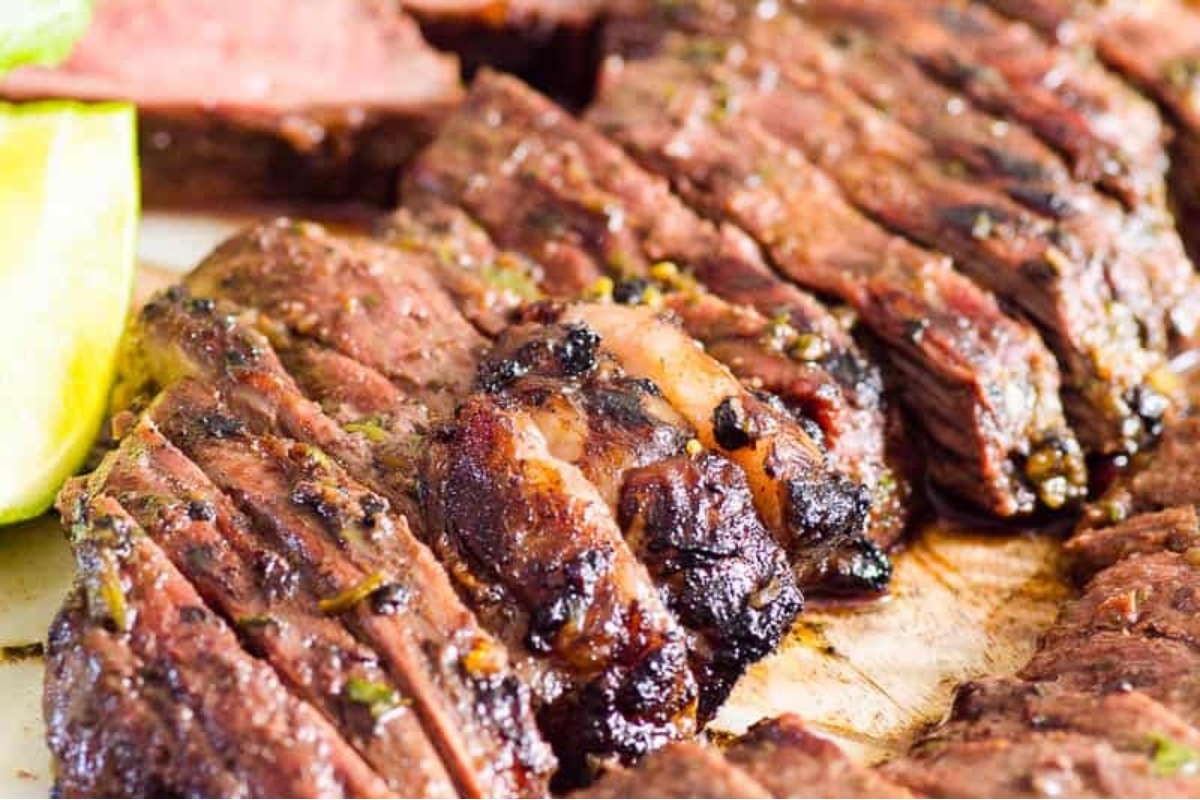 Sizzling beef steak on a cutting board garnished with lime wedges.