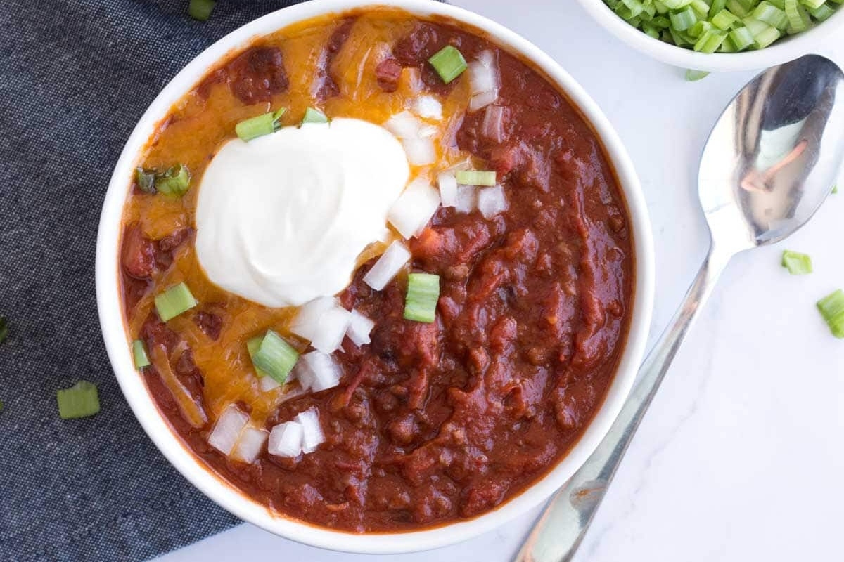 A delicious bowl of chili topped with creamy sour cream and garnished with fresh green onions.