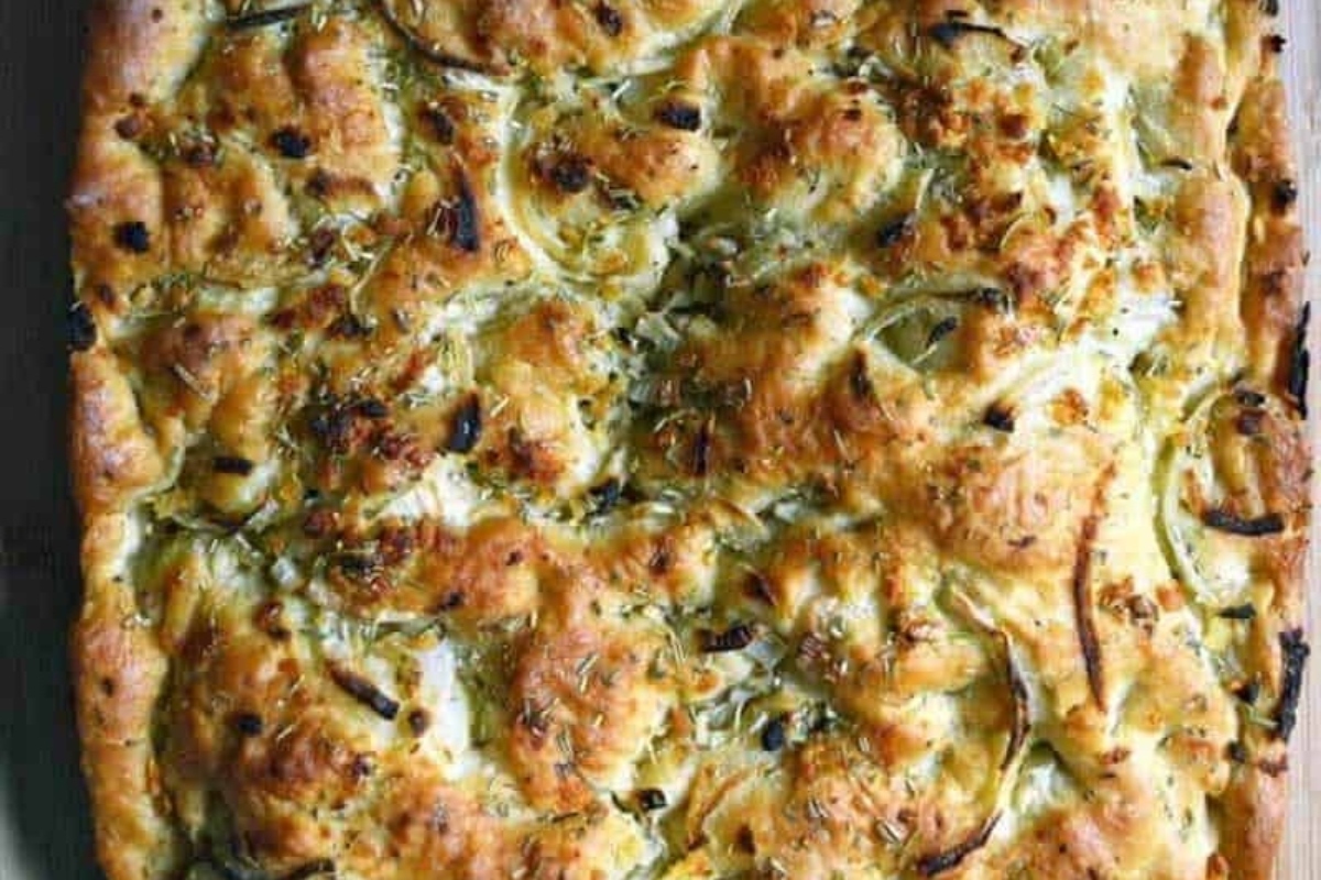 A square of bread with cheese and onions on a wooden board, perfect for creating delicious focaccia recipes.