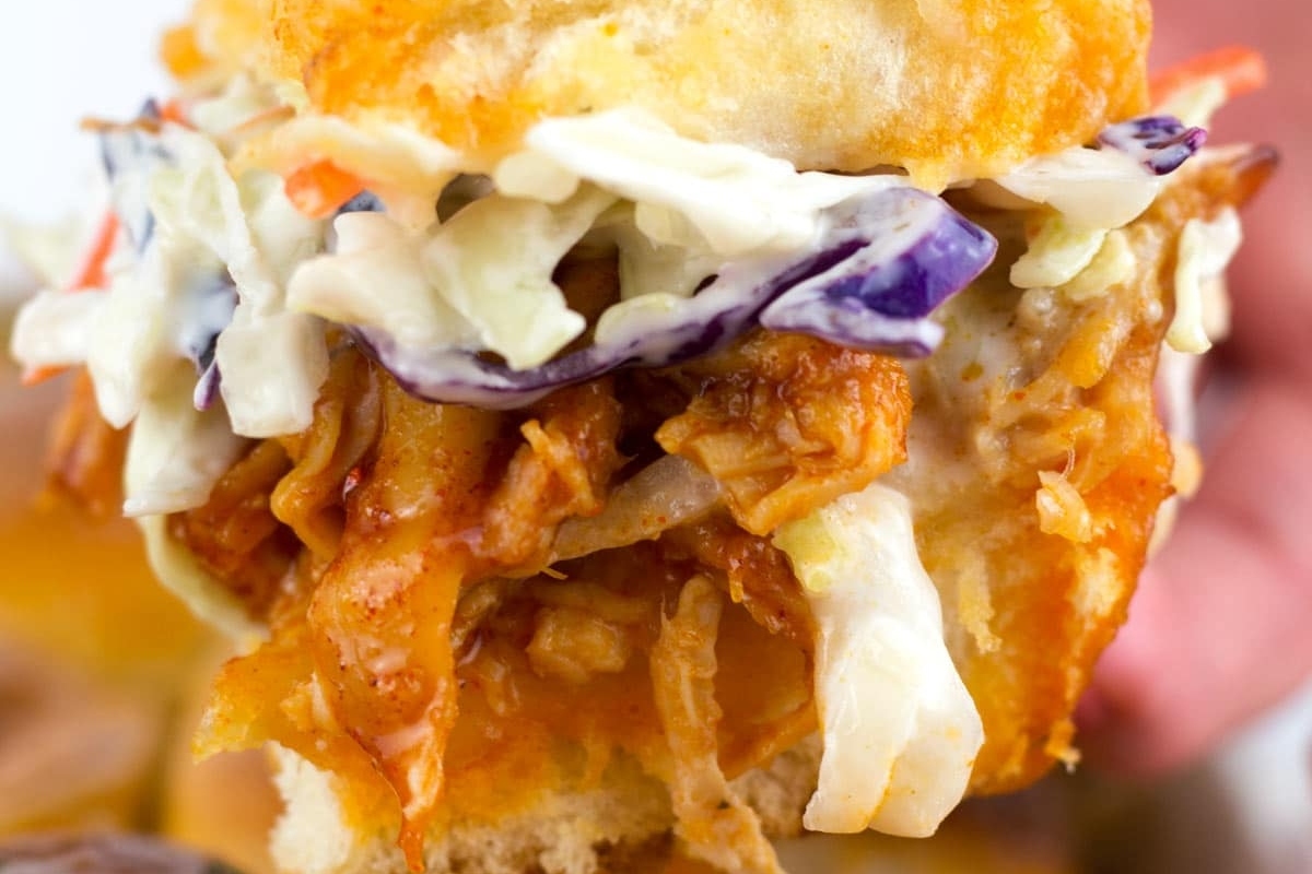 A person holding a bite-sized pulled pork sandwich with coleslaw.