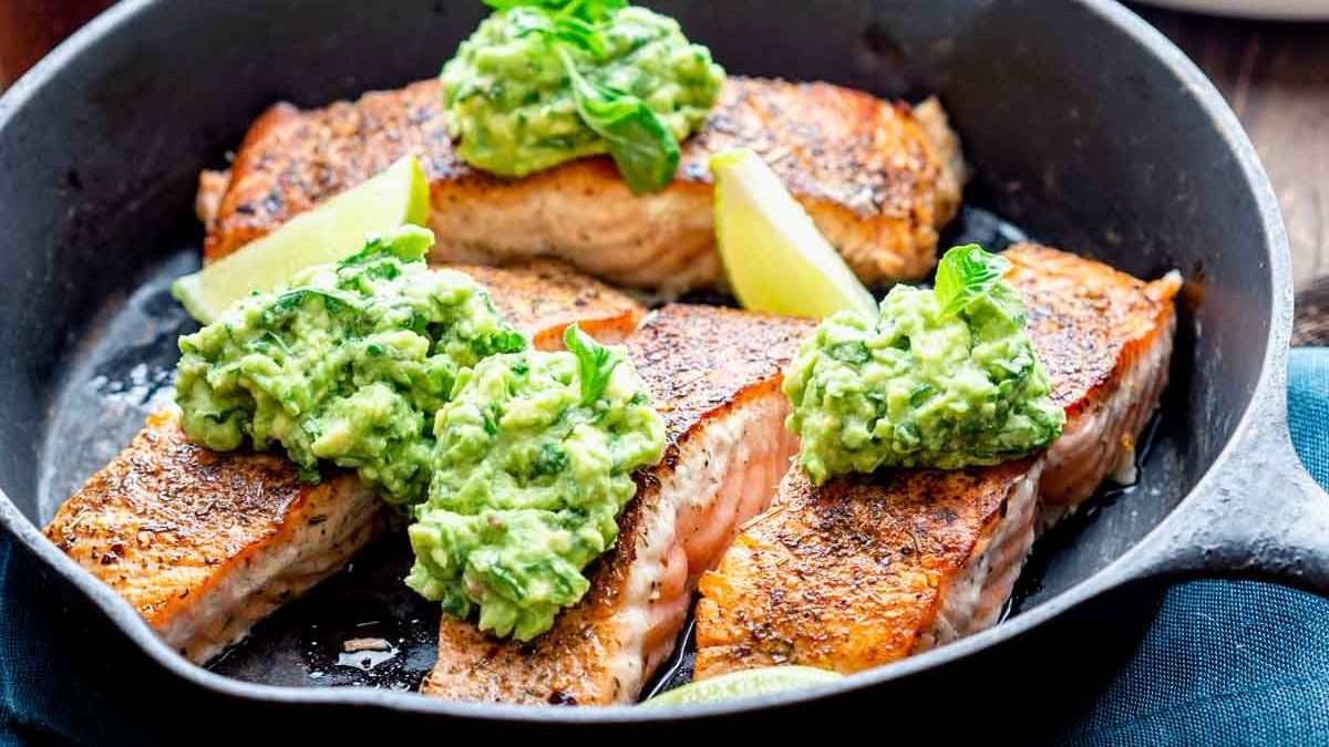 A delicious and healthy dinner option featuring tender salmon cooked to perfection in a skillet and topped with flavorful guacamole.