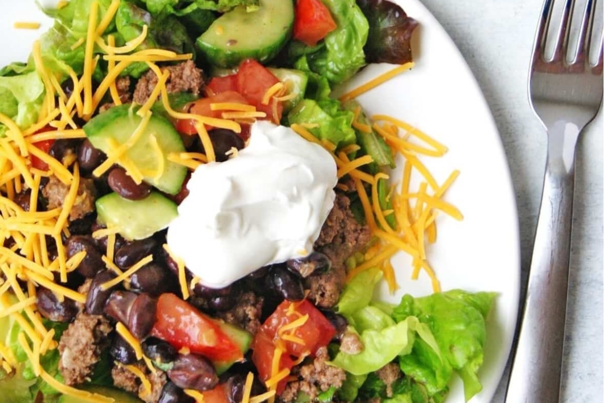 A hearty main dish salad with lettuce, tomatoes, beans and sour cream.