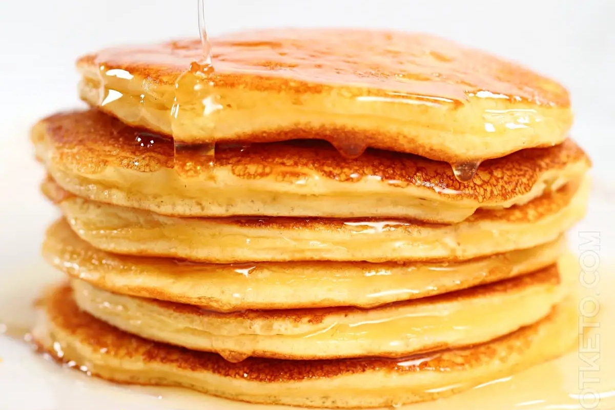 A healthy stack of high protein pancakes with syrup being poured over them.