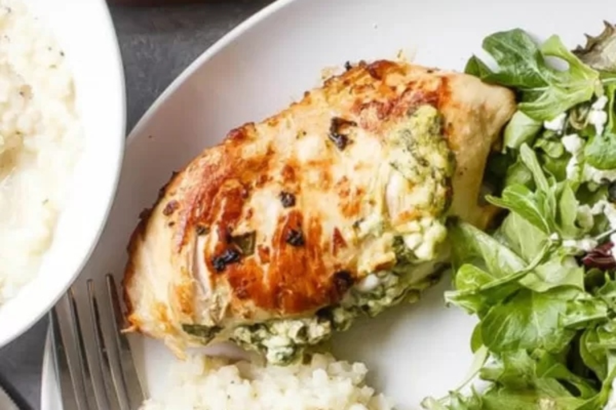 A plate with a chicken breast, spinach salad, and rice.