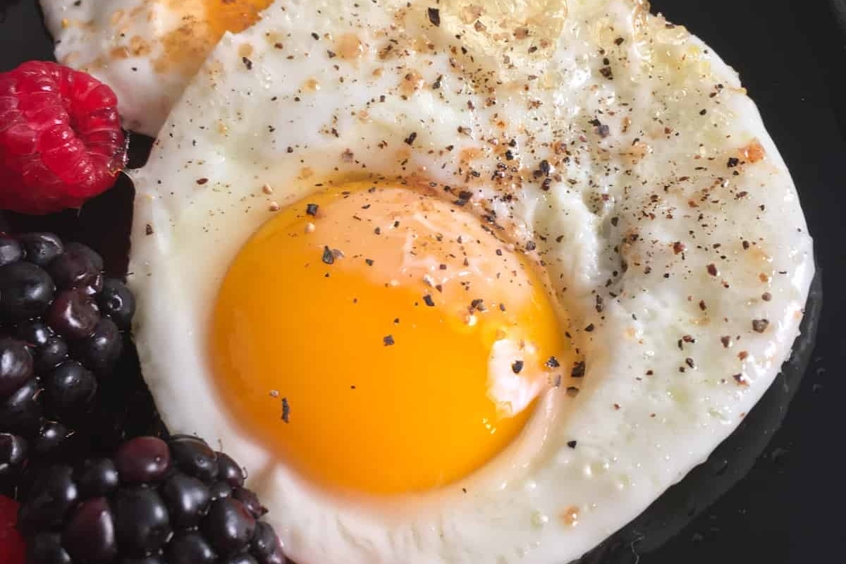 A healthy breakfast consisting of a black plate with a high protein fried egg and a side of fresh blackberries.