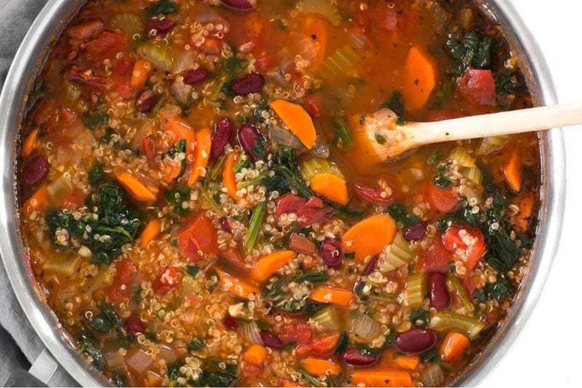 A pot full of vegetable soup with a wooden spoon.
