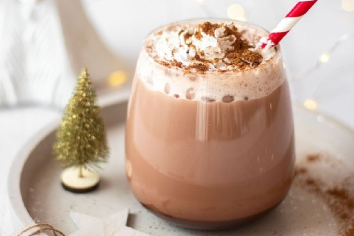 A steaming cup of hot cocoa with whipped cream and a Christmas tree.