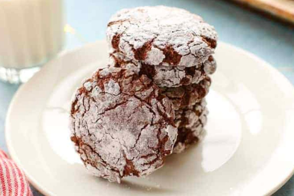 Delicious chocolate crinkle cookies on a plate next to a glass of milk, perfect for Christmas desserts.
