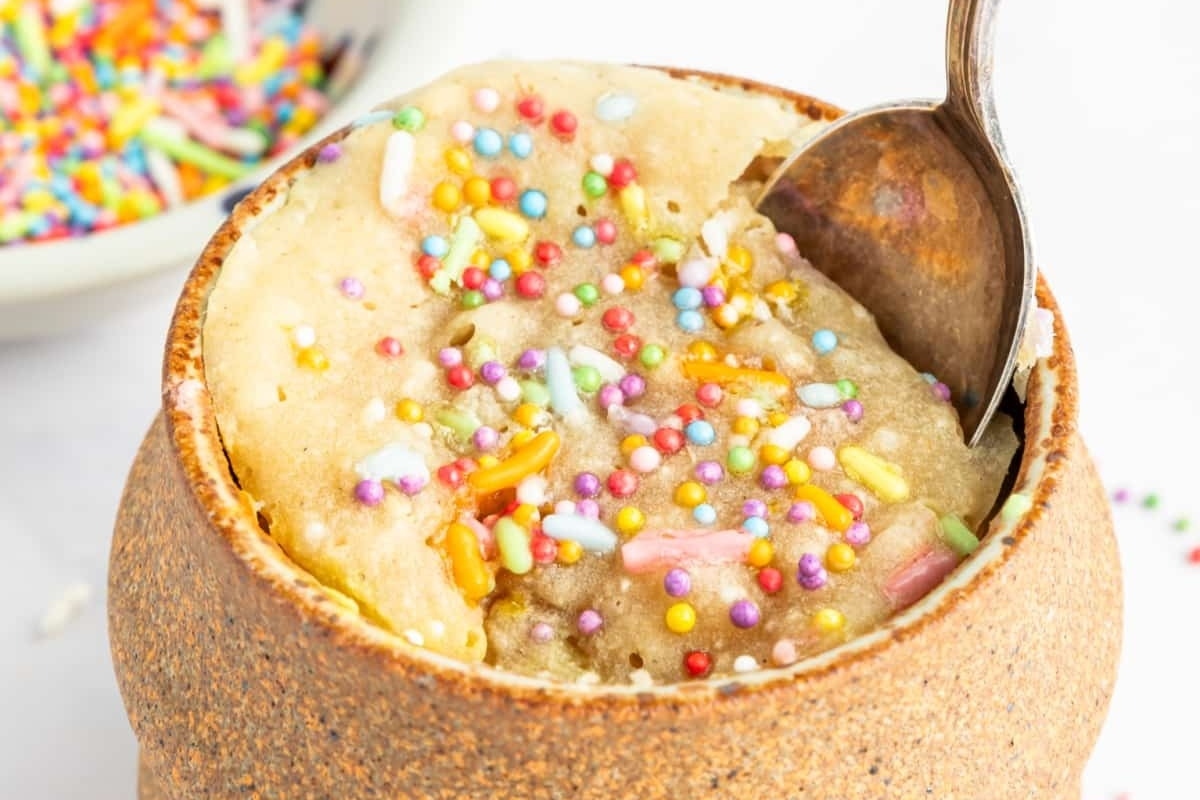 A mug filled with a spoonful of sprinkles.
