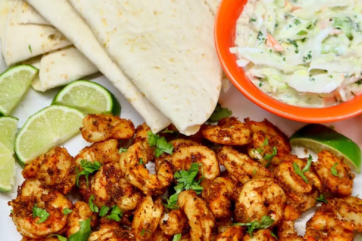 A shrimp dinner with limes and tortillas.