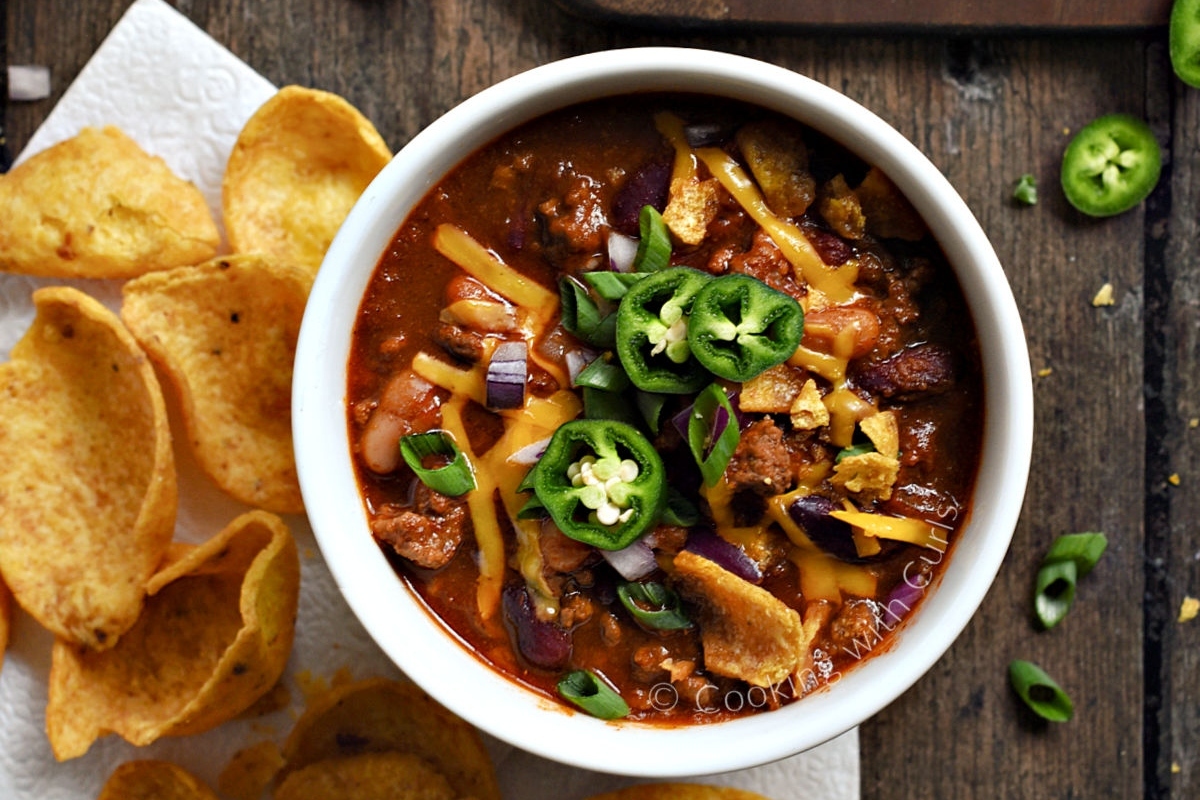 A mouthwatering bowl of chili and chips displayed on a rustic wooden table.