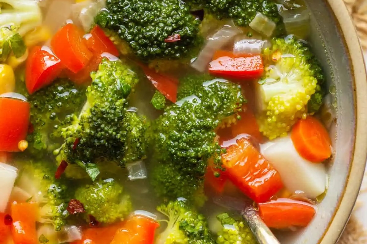 A bowl of broccoli and vegetable soup with a spoon. This recipe incorporates the nutritious and fibrous broccoli, creating a delicious and wholesome meal option.