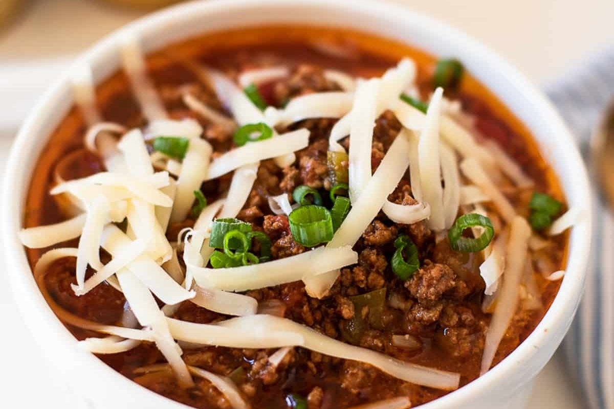 Chili recipes in a white bowl with cheese and green onions.