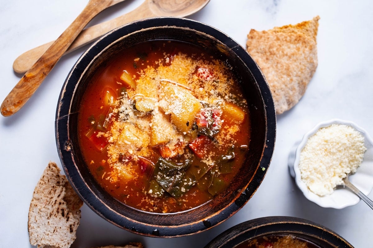 A vegetable-loaded bowl of soup served with bread and breadsticks.