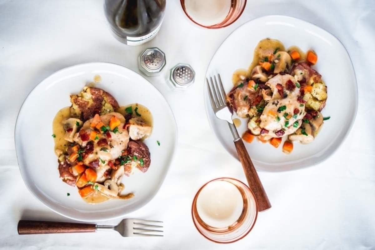 Two delicious dinners on a table next to a bottle of wine
