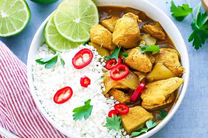 This recipe features a flavorful chicken curry served over rice and garnished with lime wedges.