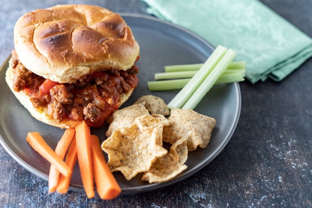 A delicious sloppy joe on a plate with carrots and celery.