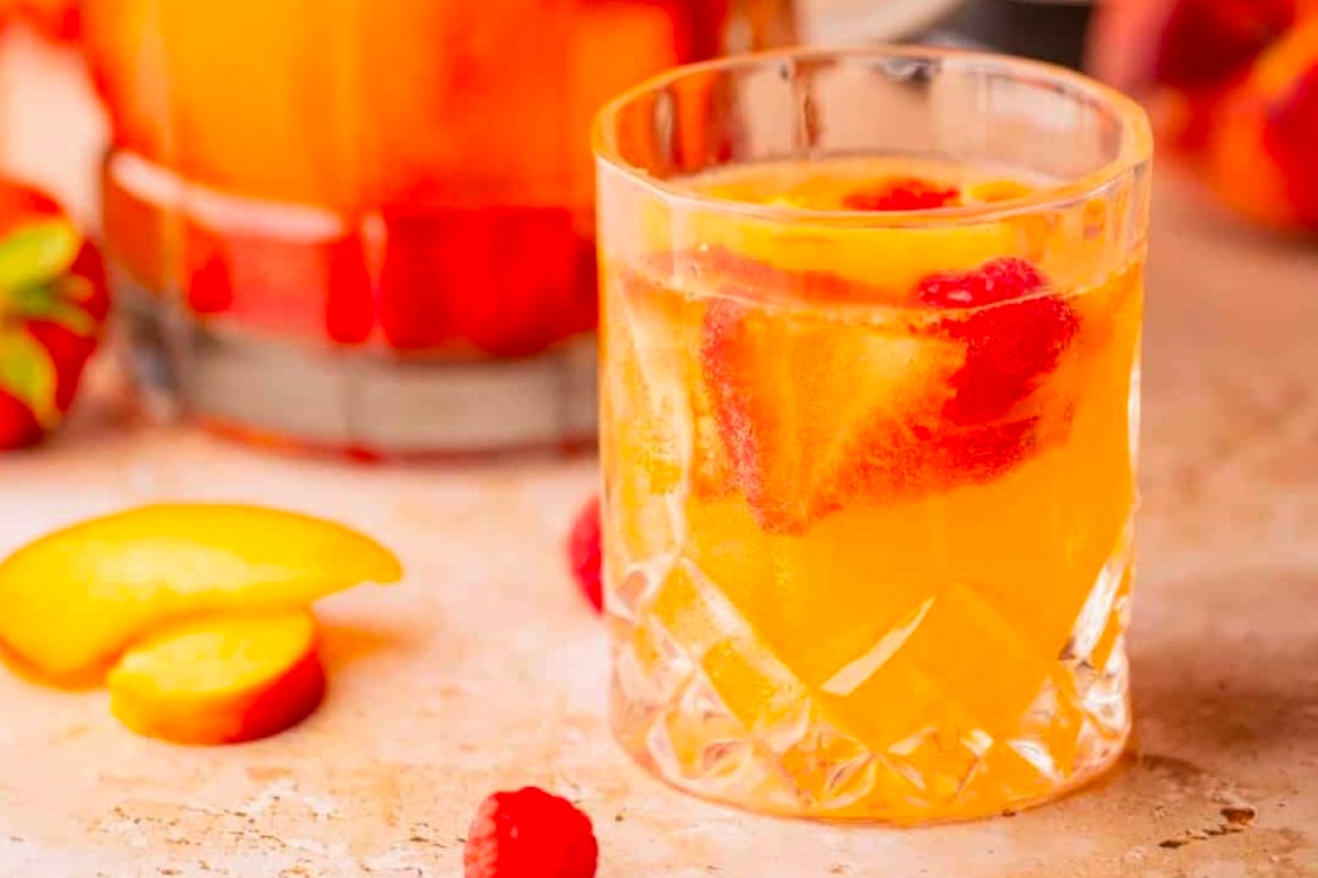 A pitcher of peach sangria alongside a glass of wine cocktails.