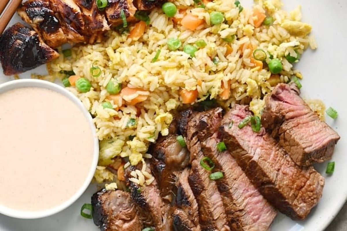A plate with steak, rice and sauce - served as a Surf or Turf delight.