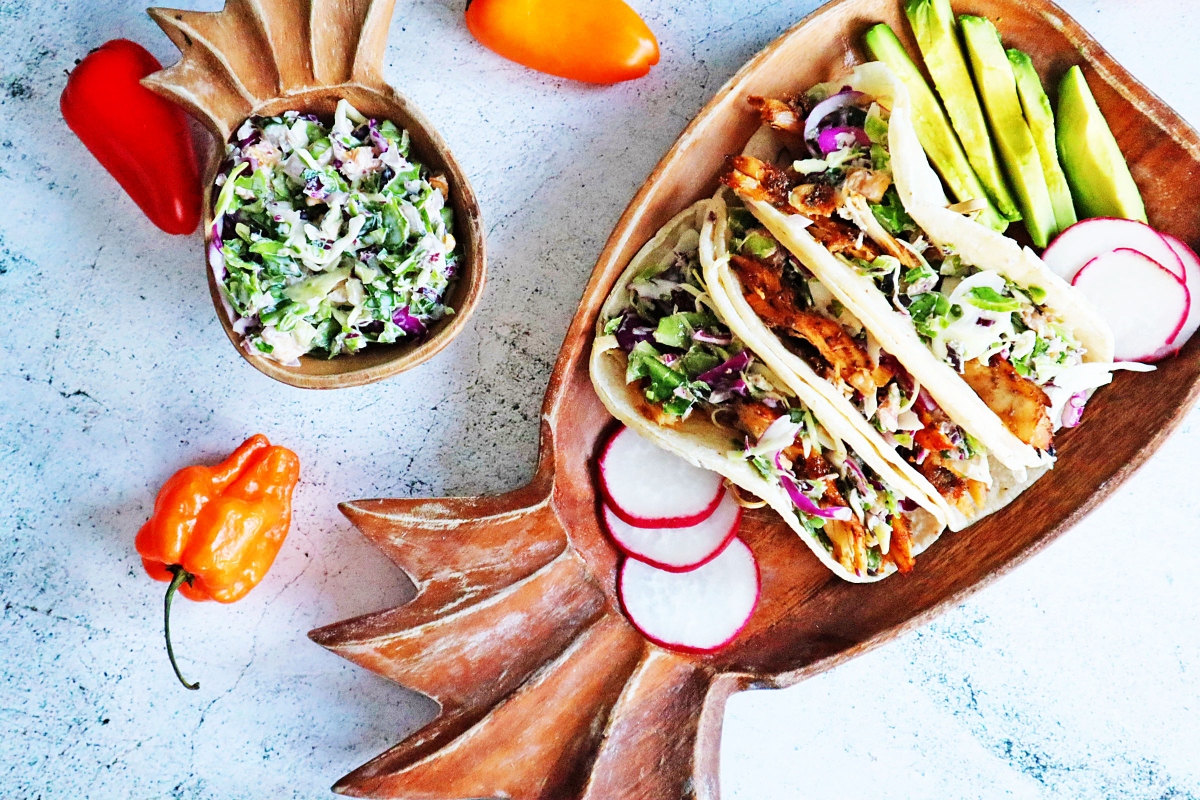 Jerk chicken tacos with slaw and radishes on a wooden plate.